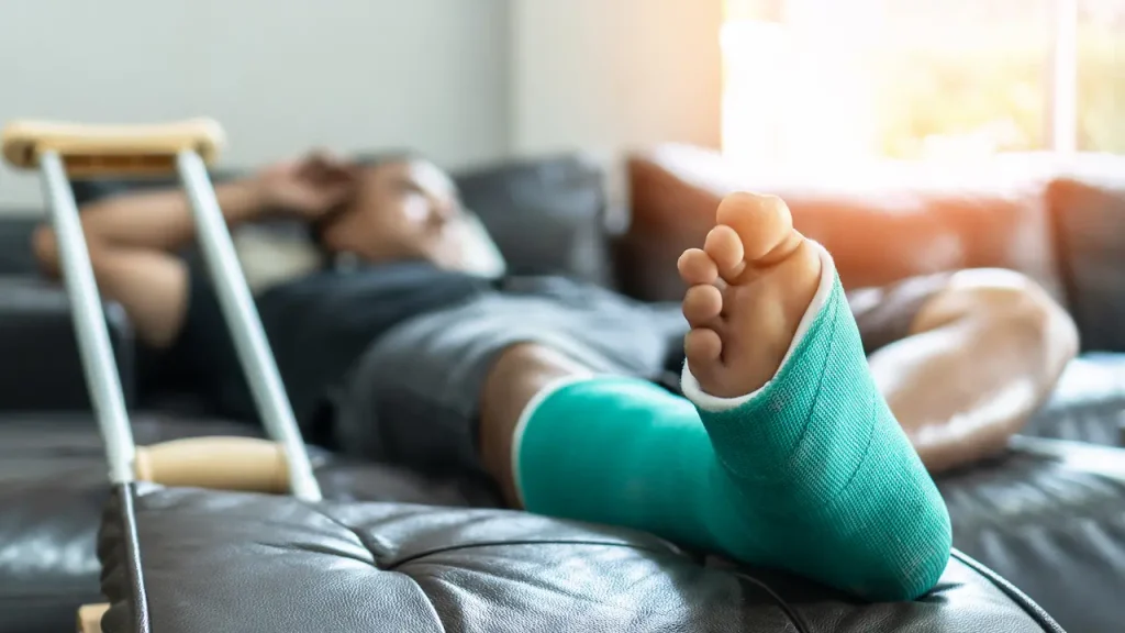 A person resting on a couch with a leg in a green cast, crutches nearby.