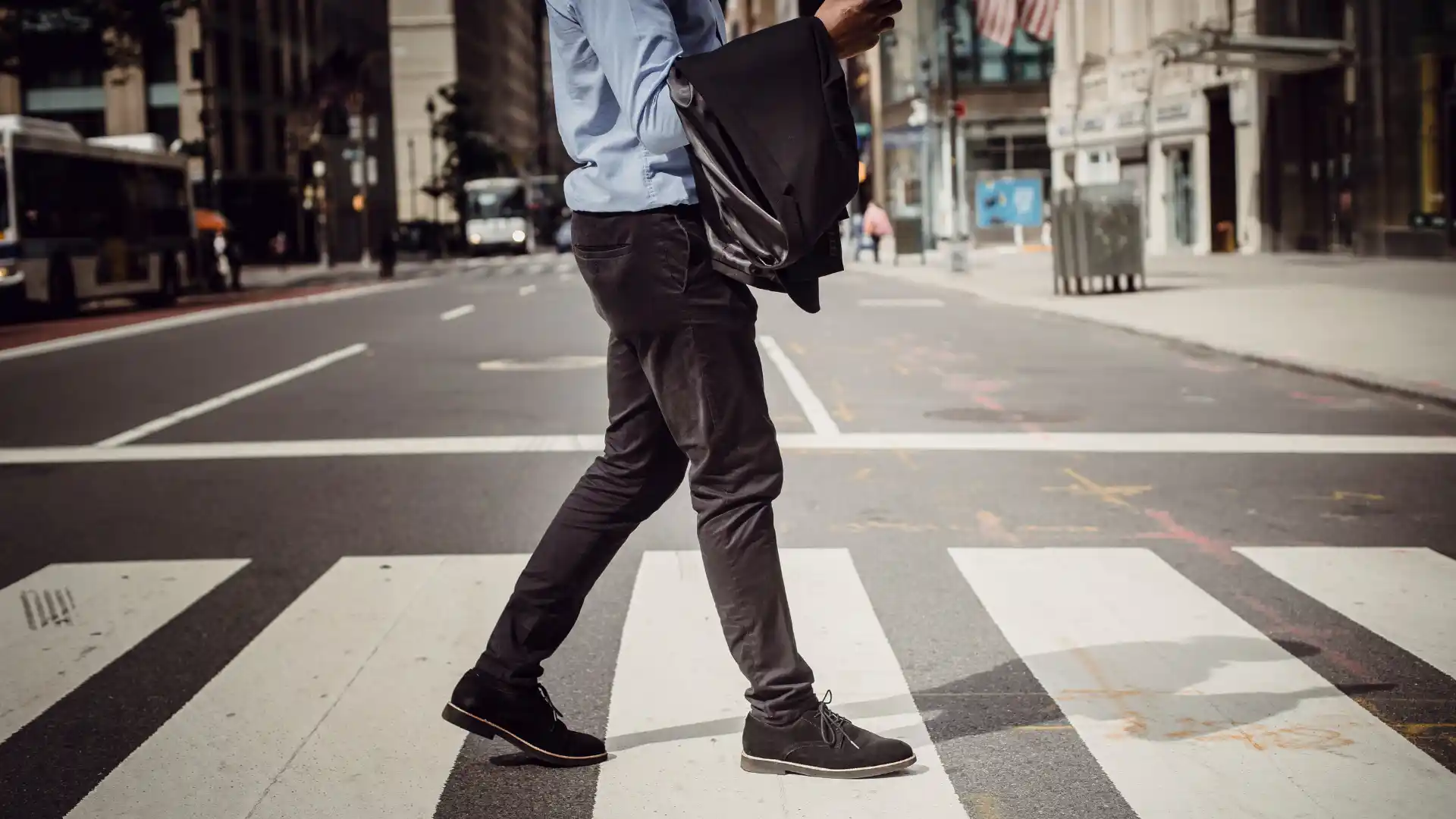 Person walking across a city crosswalk holding a jacket.