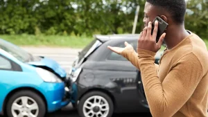 Driver on the phone after a car accident, gesturing towards the damage