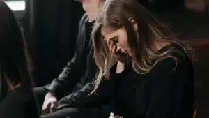 Woman with her hand on her forehead, looking distressed, sitting next to another person