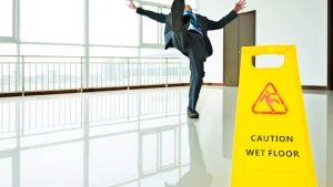 Businessman slipping on a slick floor near a wet floor warning sign.