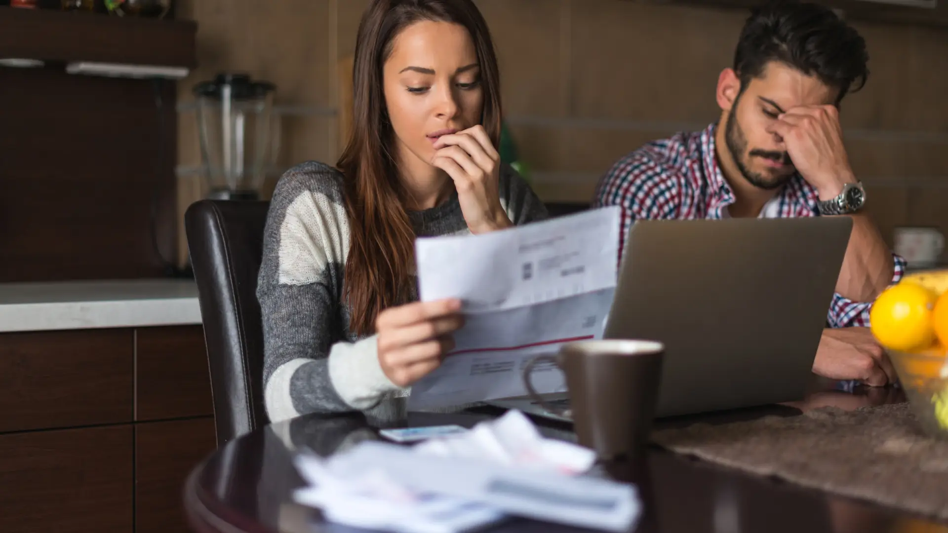 Woman reading a bill with a concerned expression, sitting at a table with a cup of coffee