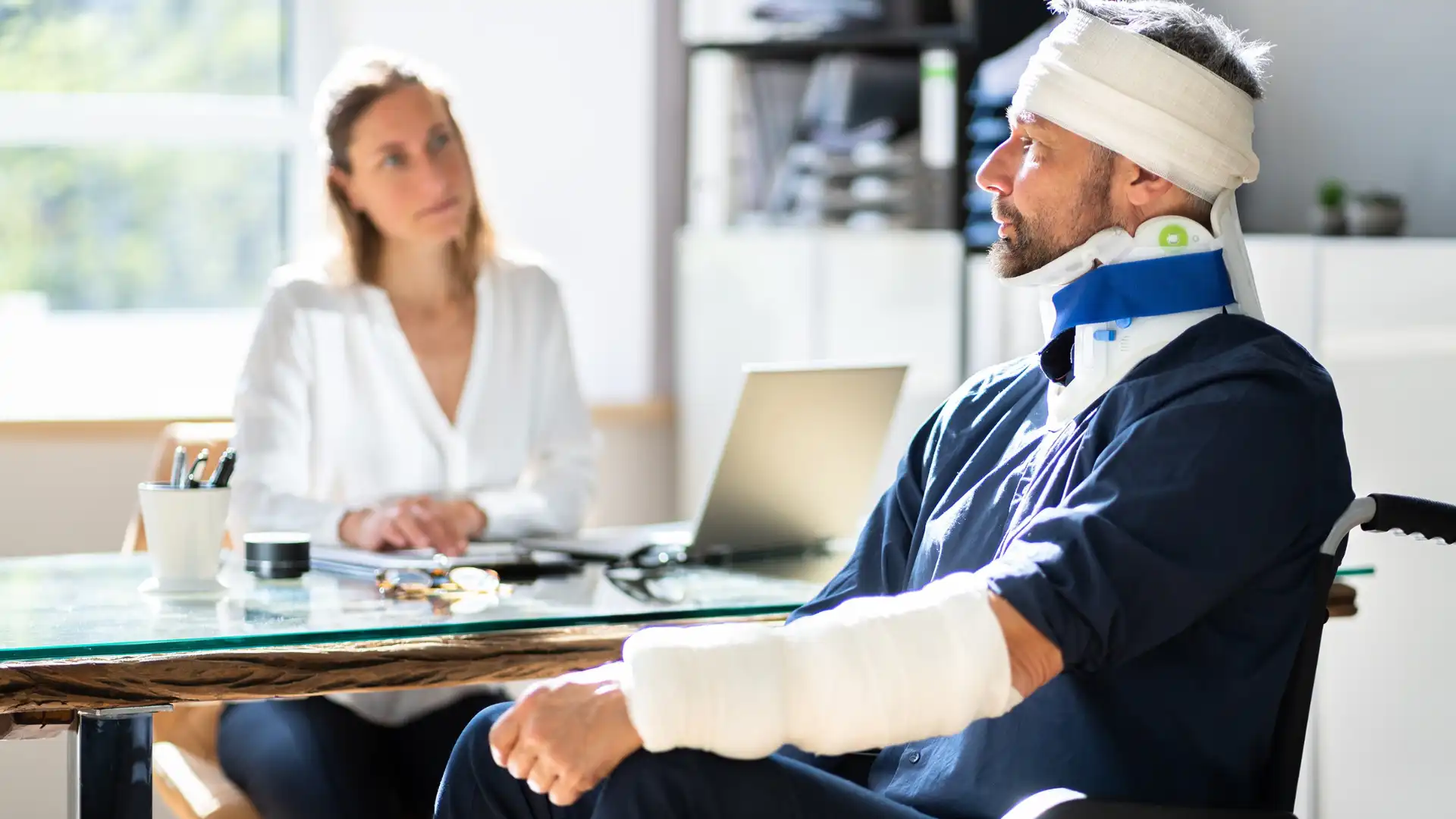 Injured man with bandages and a neck brace speaking with a female professional, possibly a lawyer or insurance representative